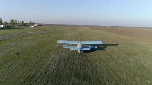 Blue Airplane Takes Off Over Field Against Sky and Horizon Line in Spring