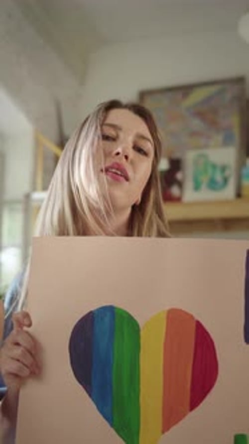 On the Foreground Two Pretty Young Girls are Standing in the Studio with a Lgbt Poster and Looking