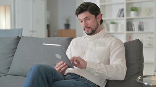 Man Using Tablet Relaxing on Gray Couch Indoors