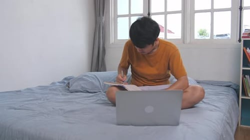 Young Adult Studying on Bed with Laptop