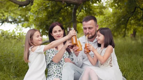 Smiling Father Mother and Two Cute Daughters Drinking Fresh Juice at Green
