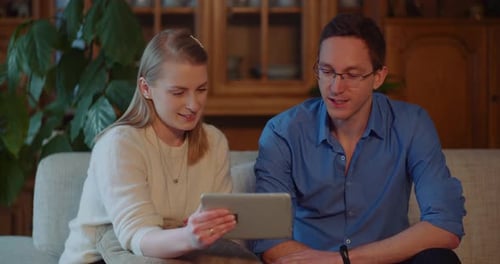 Young Adult Couple Using Tablet on Couch Indoors