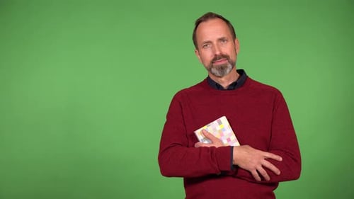 A Middleaged Handsome Caucasian Man Holds a Book and Smiles at the Camera Green Screen Background