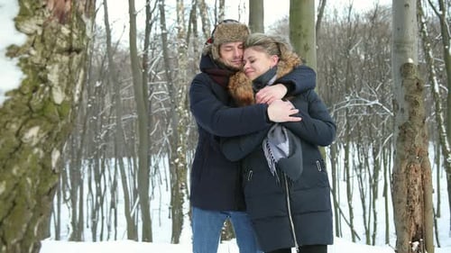 Mann umarmt Frau hautnah im verschneiten Wald