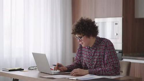 Young Adult Working at Desk with Laptop and Writing