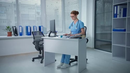 Family Doctor Works in a Hospital Office Therapist Types on a Computer Keyboard and Takes Notes