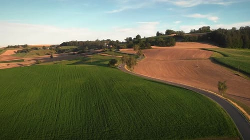 Cars driving on winding asphalt road through fields and meadows at sunset