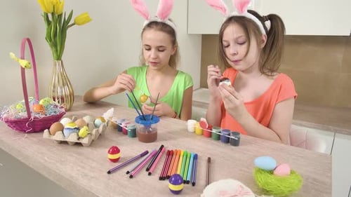 Mädchen mit Hasenohren auf dem Kopf verzieren Ostereier mit Farbe