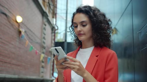 Slow Motion of Beautiful Girl with Curly Hair Using Smart Phone Messaging Standing Outdoors in City