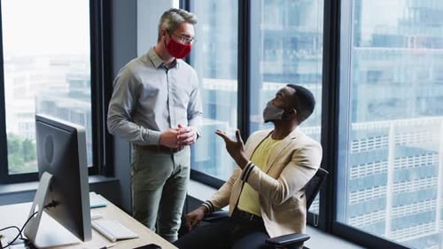 Diverse male office colleagues wearing face masks discussing at modern office