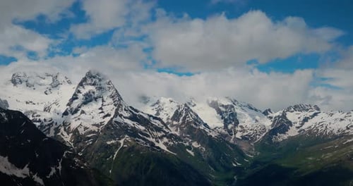 Air Flight Through Mountain Clouds Over Beautiful Snowcapped Peaks of Mountains and Glaciers