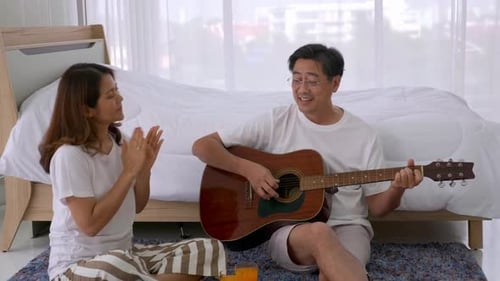 Man Plays Guitar for Woman Indoors
