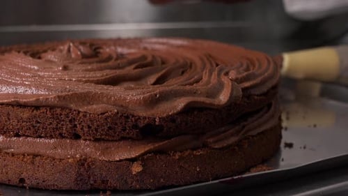 A Baker Puts a Layer Onto a Dark Cake Base with Chocolate Frosting - Closeup