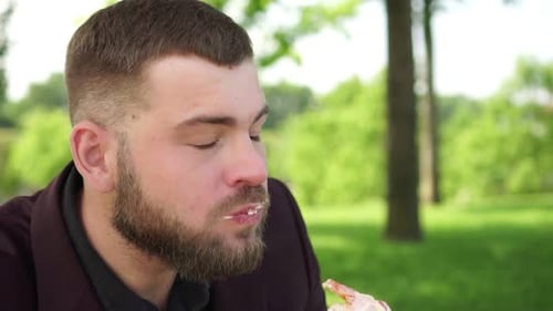 Man Enjoying a Sandwich Outdoors in Park