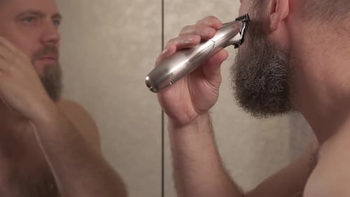 Man shaving beard using electric trimmer shaver. Male beauty grooming concept.