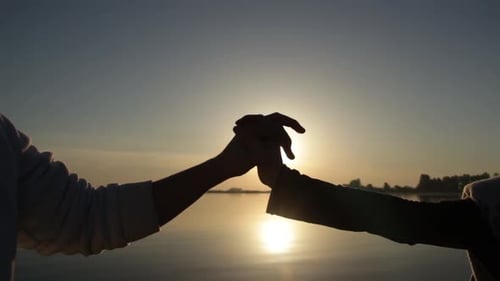 Friends Grasping Hands at Sunset on Calm Water