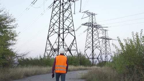 Electrical Engineer Walking toward Power Transmission Towers