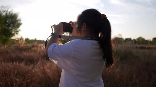Back view of girl standing in meadow and taking a picture by camera