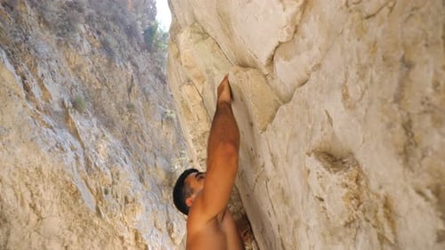 Junger muskulöser Mann klettert vorsichtig am Felsen. Starker Kerl, der auf Rock Peak aufsteigt