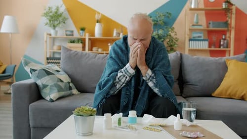 Slow Motion of Unhealthy Old Man Coughing Sitting on Couch at Home Taking Medicine