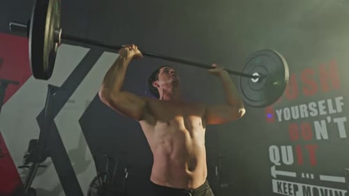 Joven atleta o deportista caucásico sin camisa, hace ejercicio levantando una barra o levantando pesas en el gimnasio.