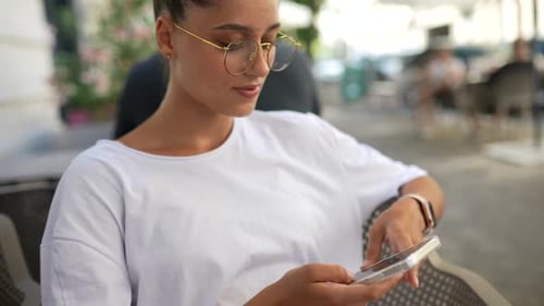 Beautiful Young Woman Sitting in Street Cafe Using a Smartphone