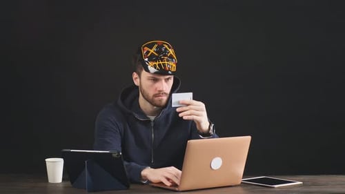 Masked Young Adult Using Laptop with Card
