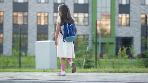 Preschooler Girl with Schoolbag Walks Past School Building