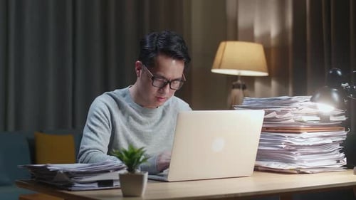 Man Working Late at Laptop with Documents