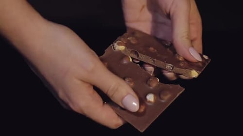 Woman Breaks Black Chocolate Bar with Nuts