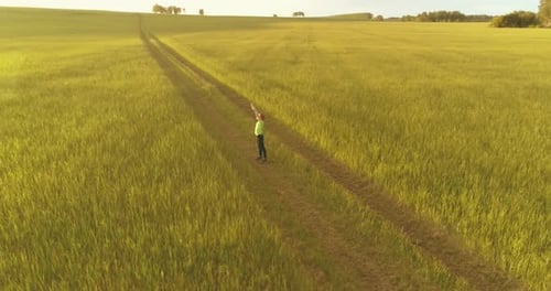Sporty Child Standing in Green Wheat Field with Raised Hands Up