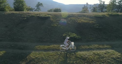 Shot of a Young Womanin a Light Dress and Hat Riding Bicycle on Rural Road