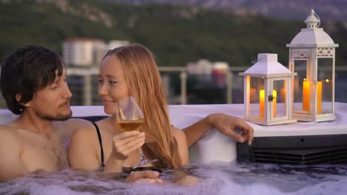 A Young Man and Woman are Relaxing in the Hot Tub on a Rooftop with a View on Mountains During