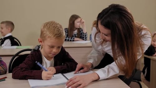 Teacher Helping Young Boy with Writing Lesson in Elementary School