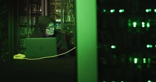 Hacker asiático masculino com capuz usando laptop em servidores de computador