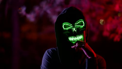 Portrait of a Person in a Terrible Glowing Mask of Death and in a Dark Hood Against a Background of