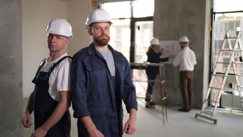 Dos constructores con cascos posando en el lugar de trabajo
