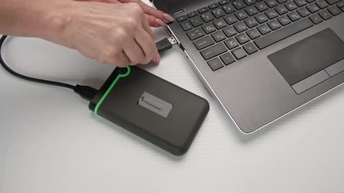 Jovem mulher insere um disco rígido portátil em um laptop em um plano de fundo claro