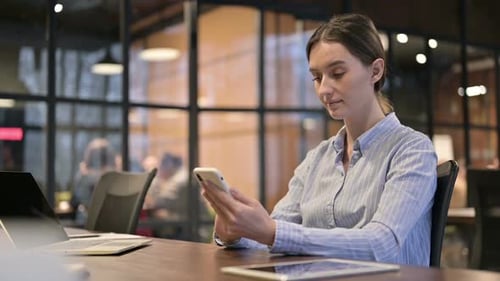 Young Woman Using Smartphone at Desk in Office