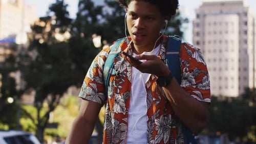 African american man in city, wearing earphones, talking on smartphone in the street