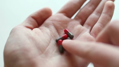 Man takes and shows pills vitamins or drugs tablets in hand from pill bottle