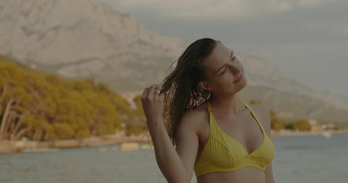 Jeune femme aux cheveux mouillés en maillot de bain sur la plage au coucher du soleil