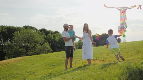Family Flies Kite on Grassy Hillside