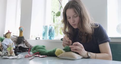 Woman Crafting Small Green Stuffed Toy at Desk