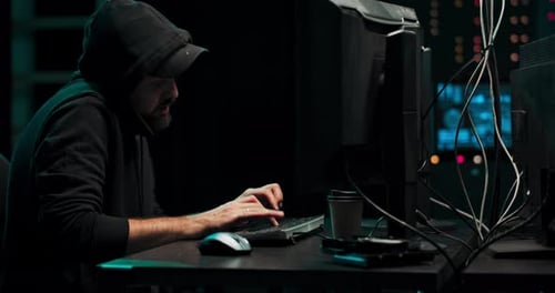 Hooded Man Typing on Computer in Dark Office
