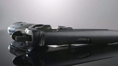 Waffenkontrolle. Studioaufnahme einer 9-mm-Pistole, die sich auf einer reflektierenden Oberfläche dreht