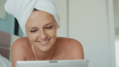 Smiling Woman Using Tablet in Bed at Home