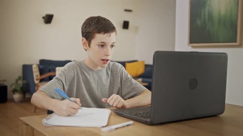 Boy Studies and Writes at Table with Computer