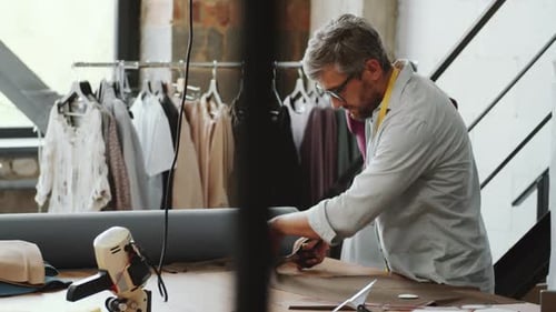 Male Tailor Cutting Fabric with Scissors at Work in Sewing Studio