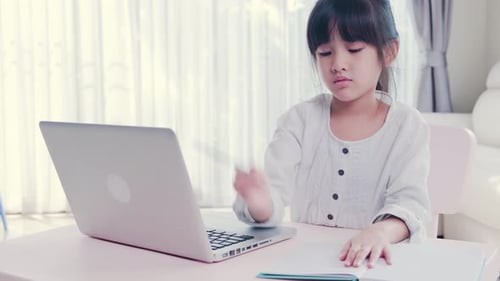Asiatisches junges Studentenkind, das von zu Hause aus lernt und im Wohnzimmer eine kurze Notiz auf ein Papierbuch schreibt.